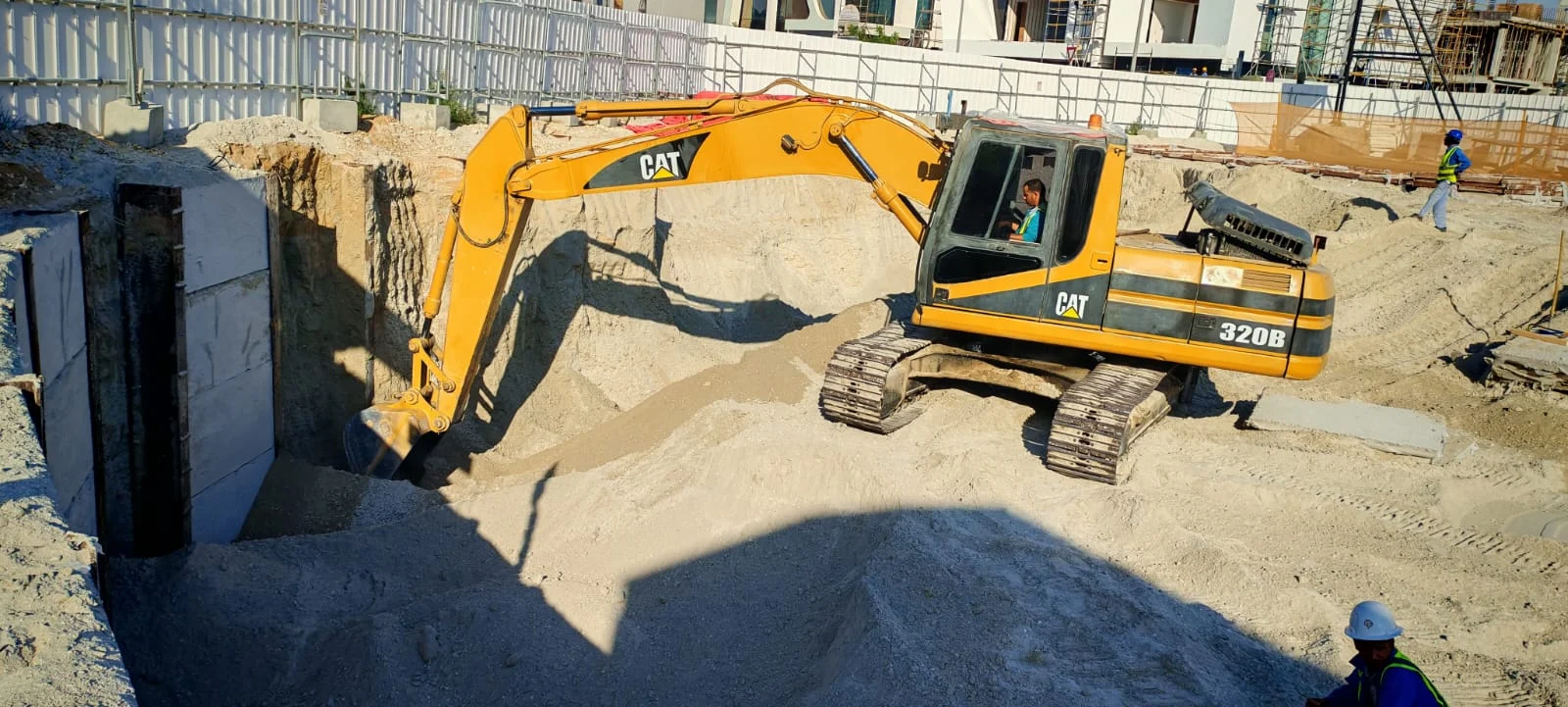 Excavator removing sand within concrete-panel shoring